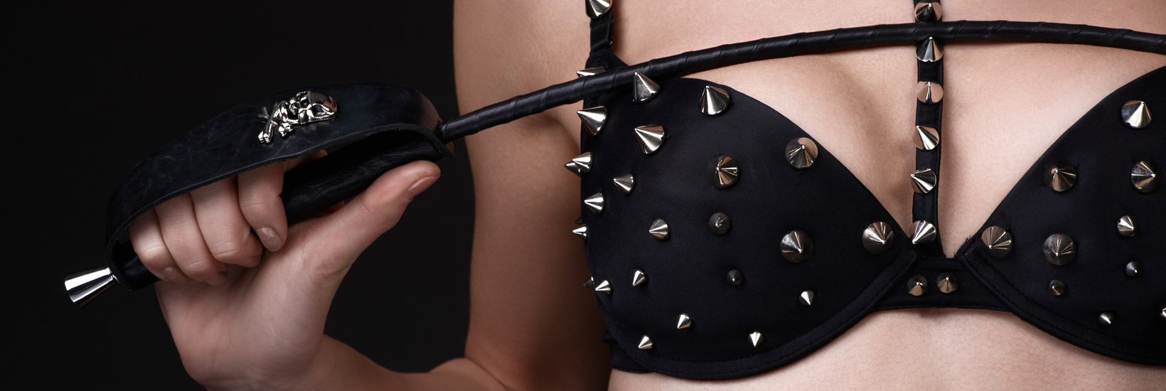 BDSM Frau in schwarzen Dessous mit Nieten und Peitsche